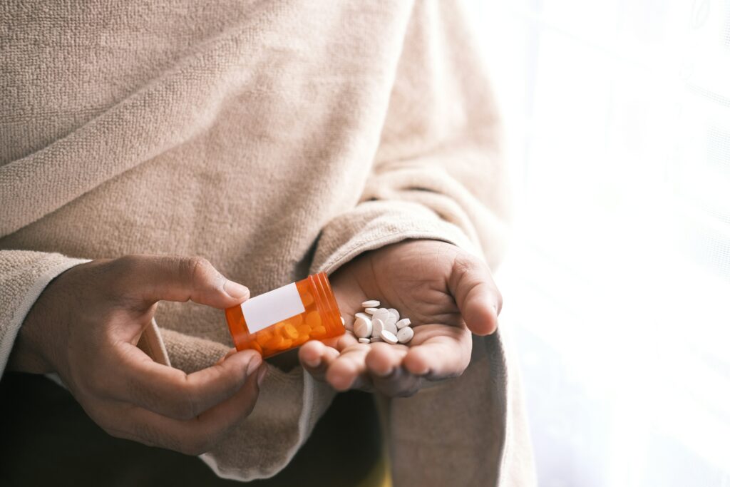 A zoomed in photo on someone’s hands, pouring a bottle of pills into one hand while holding the bottle with the other.